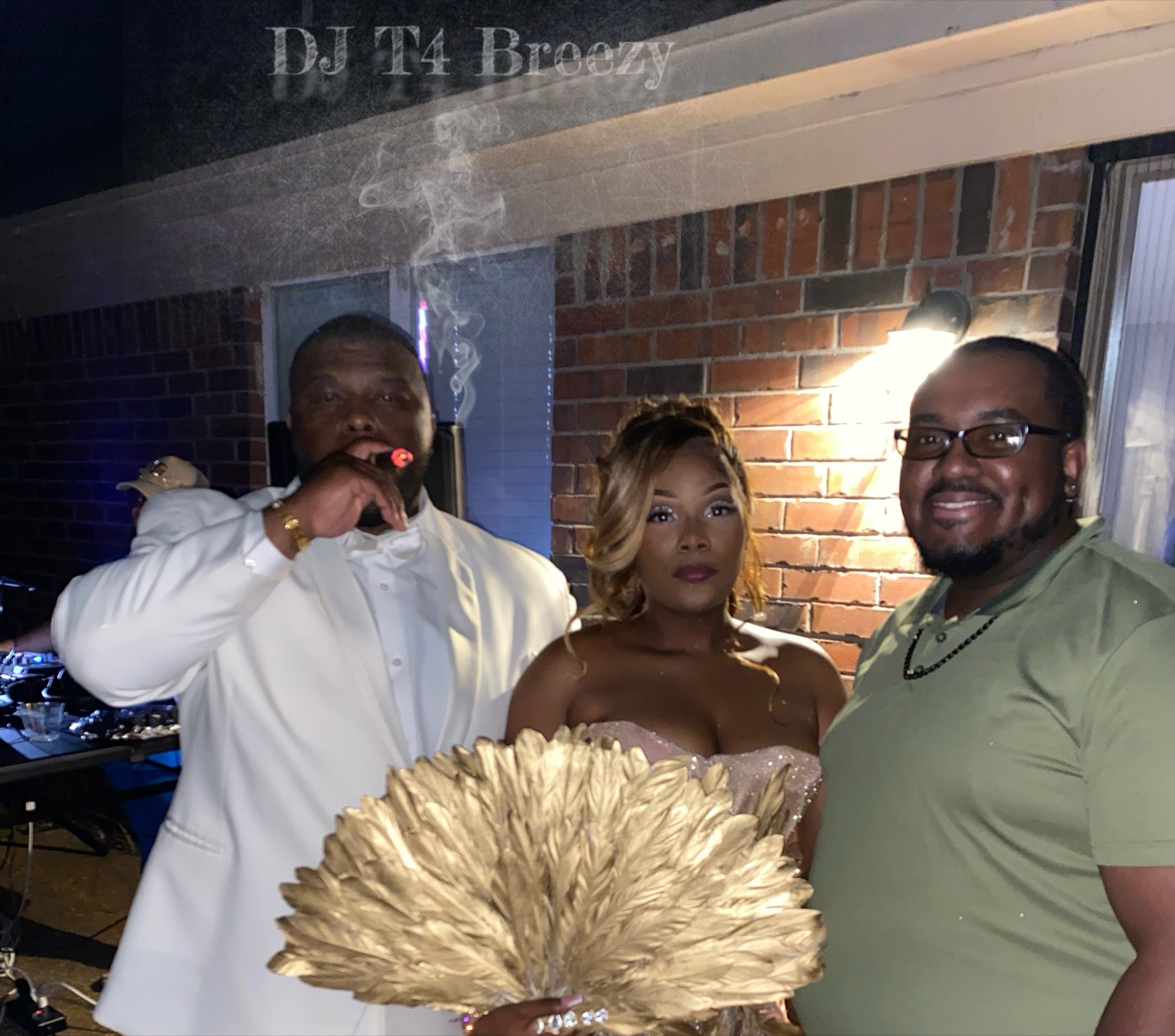 DJ T4 Breezy with guests in formal wear, one holding a gold feather fan, beside the DJ booth
